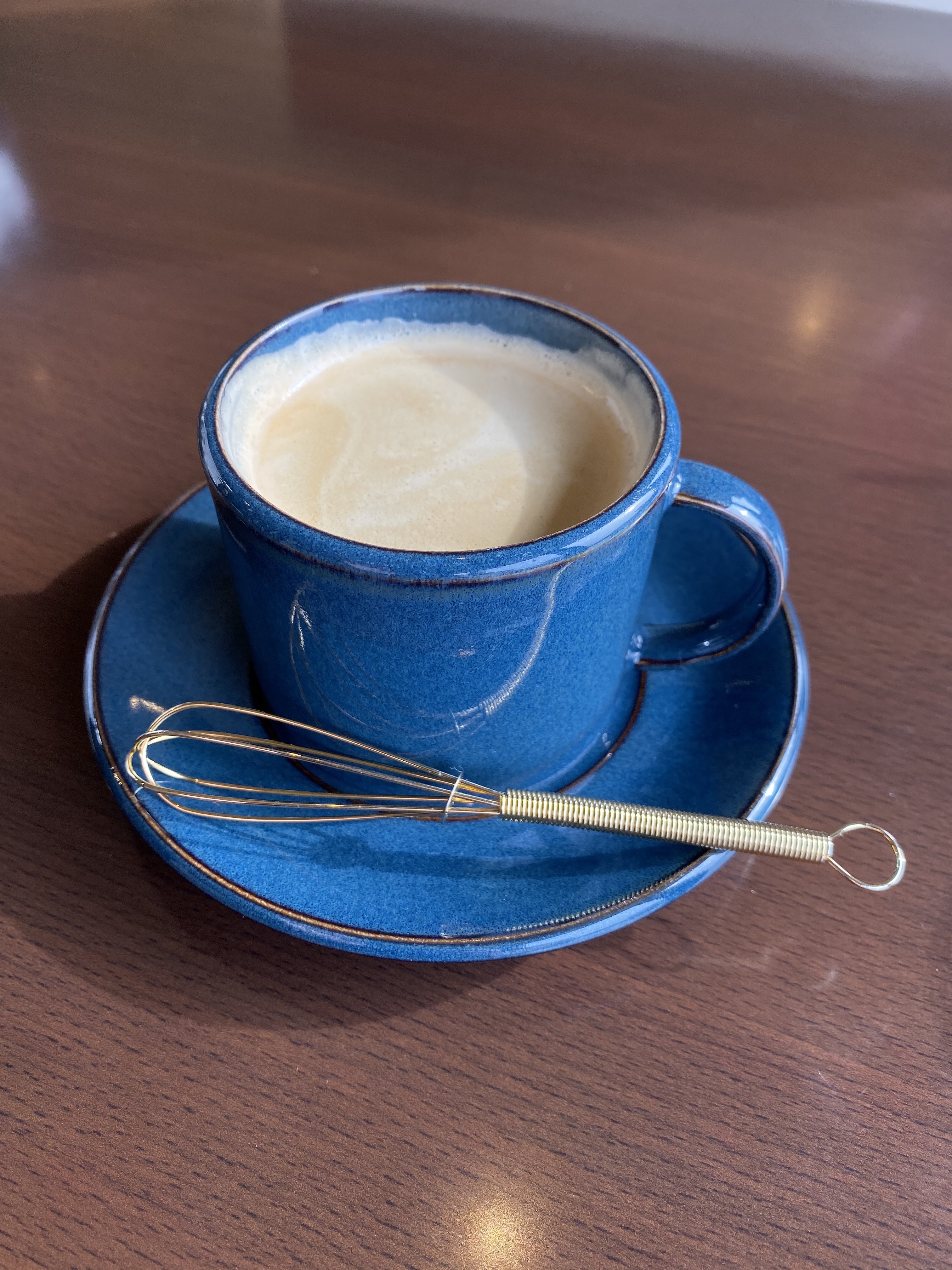 Foamy coffee with a royal blue ceramic mug and gold wisk